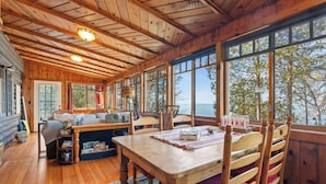 Un interno accogliente di una baita con un tavolo da pranzo in legno, sedie e una grande finestra vista su una zona boschiva.