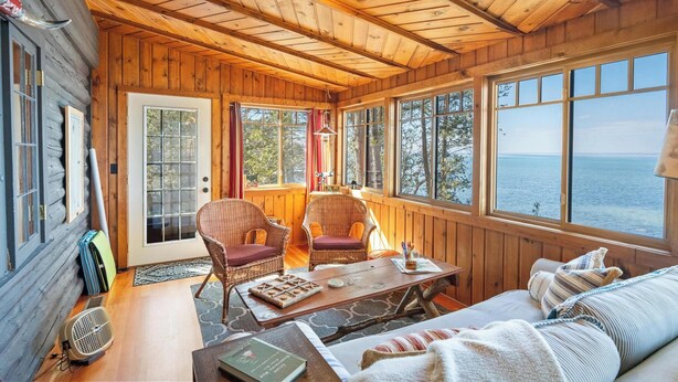 L'interno accogliente di un rifugio con soffitto in legno, ampie finestre, mobili in vimini e vista mare.