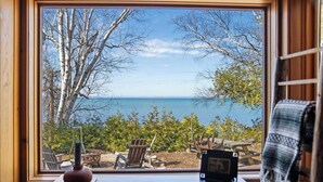 Vista dalla finestra su una spiaggia, con sedie e un tavolo di legno, un cactus e una coperta sul lato destro.