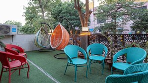 A patio with wicker chairs, a hanging chair, and a table with a lantern. - The Ansal (Greater Noida)