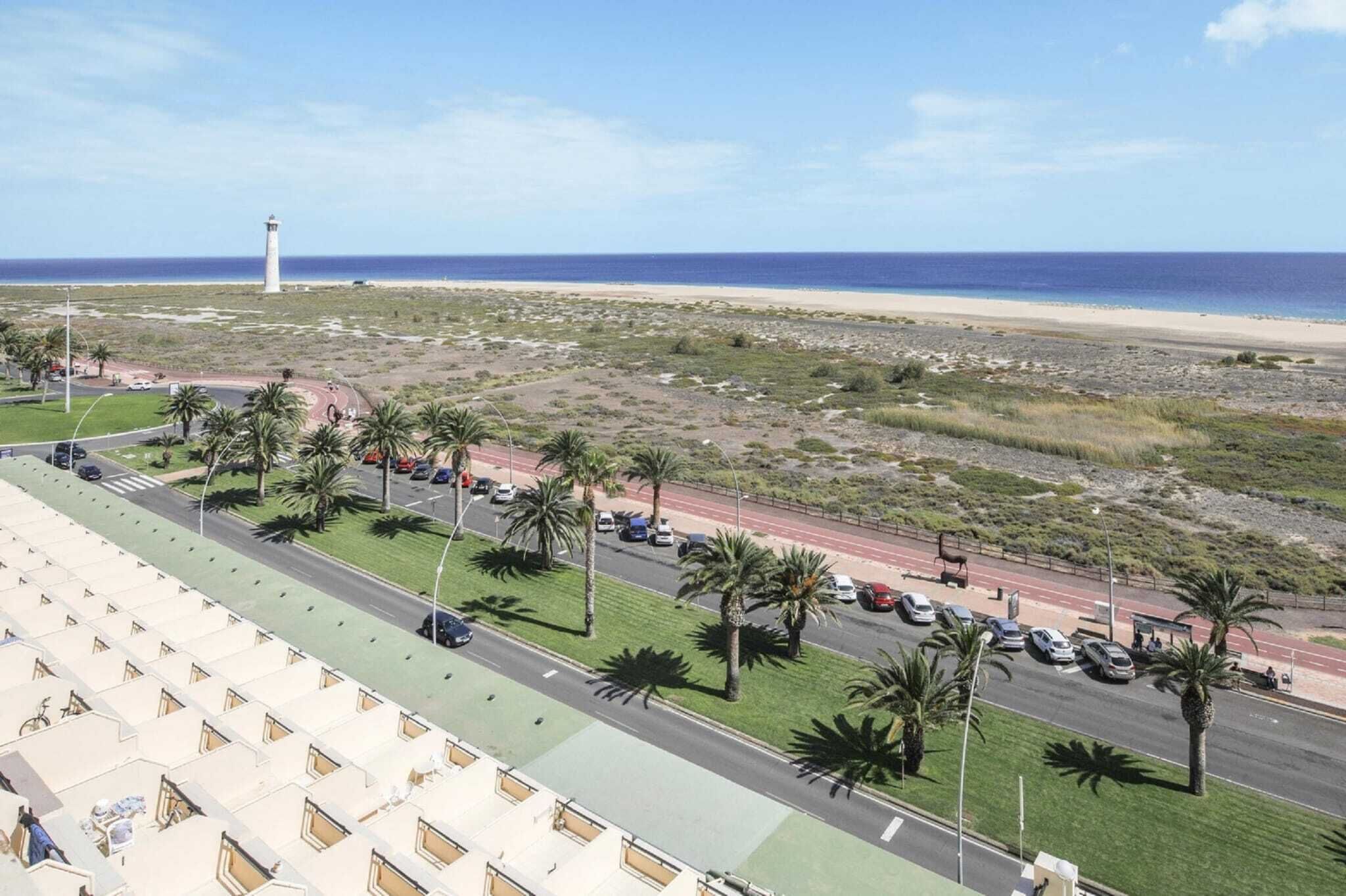 A coastal road with a beach in the background, palm trees, and a lighthouse.