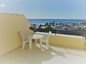 Enjoy a tranquil beach view from this balcony with a table and two chairs.
