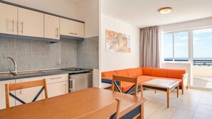 Een ruimtelijk ingerichte leefruimte met kitchenette, eethoek en een bank met uitzicht.