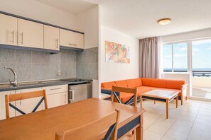 Enjoy a compact living space with a kitchenette and seating area, featuring a stove, sink, cabinets, sofa, and table.