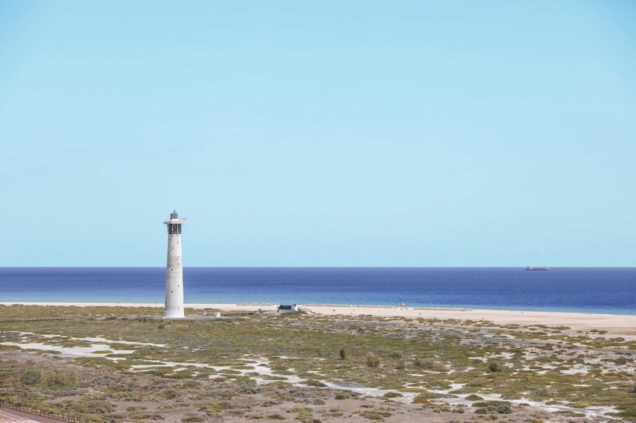 A lighthouse on a beach with a clear sky and calm sea.