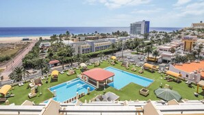 Een resort met een groot zwembad, palmbomen en uitzicht op het strand.