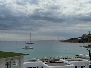 A coastal view with boats on the water, a lighthouse, and buildings on a hillside.