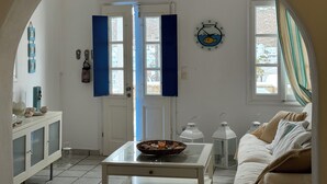 Una habitación con una puerta blanca, un reloj de pared con motivos de peces, un sofá blanco, una pequeña mesa con una cesta y un armario blanco.
