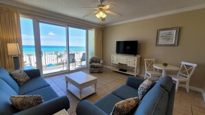 A living room with a large sofa set, a television on a cabinet, a ceiling fan, and a view of the beach through the sliding glass doors. - Family-Friendly Condo, Amenities Galore (Panama City Beach)