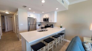 A modern kitchen with white cabinets, stainless steel appliances, a large island with bar stools, and a blue couch in the adjacent living area. - Family-Friendly Condo, Amenities Galore (Panama City Beach)
