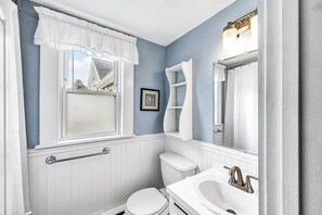 Une salle de bain avec des toilettes blanches, un lavabo blanc, une fenêtre avec un rideau blanc et un radiateur blanc.