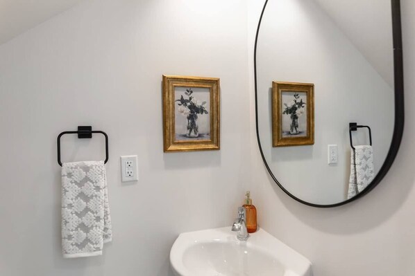 Een badkamer met een wit wastafelmeubel, een spiegel en twee ingelijste foto’s aan de muur.