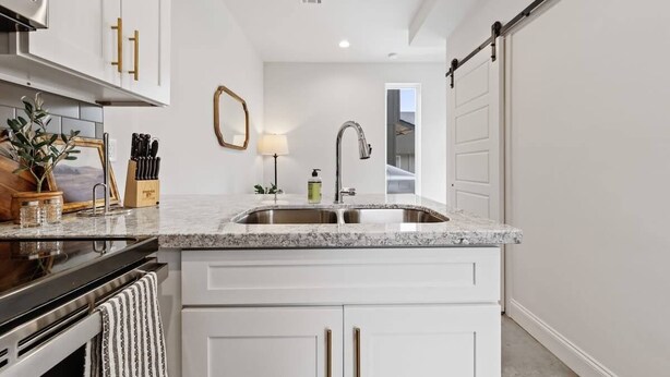 A kitchen with white cabinets, a granite countertop, a stainless steel sink, and a sliding door.