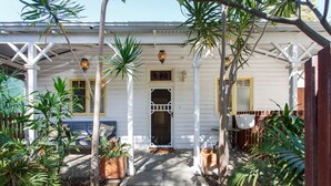 A white house with a porch, potted plants, and a wooden fence.