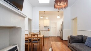 A compact living space with a dining area, a sofa, a wooden table, and a kitchen in the background.