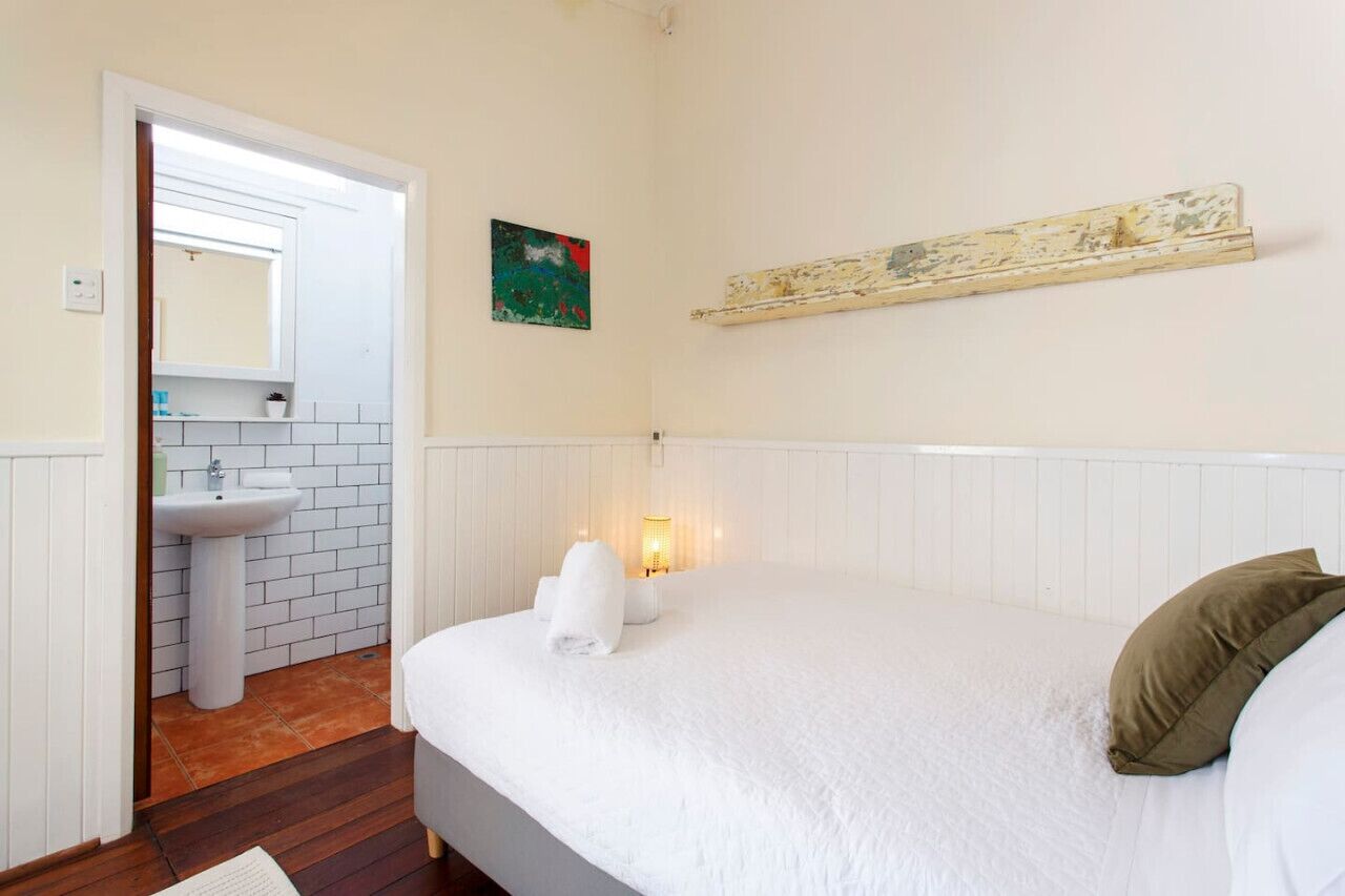 Ein Schlafzimmer mit einem Bett, einer Nachttischlampe, einem Wandregal, einer Tür zu einem Badezimmer und einem kleinen Gemälde an der Wand.