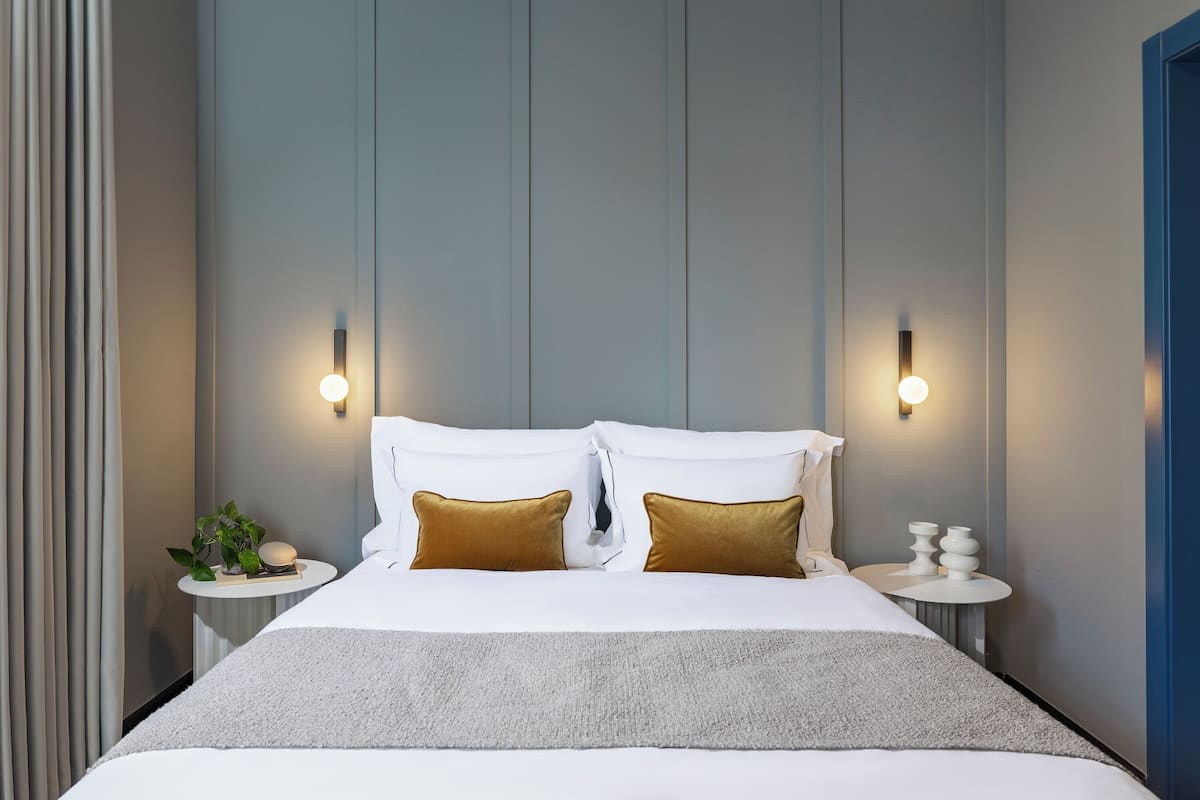 A modern hotel room with a large bed, two bedside tables with lamps, and a wall-mounted light fixture.
