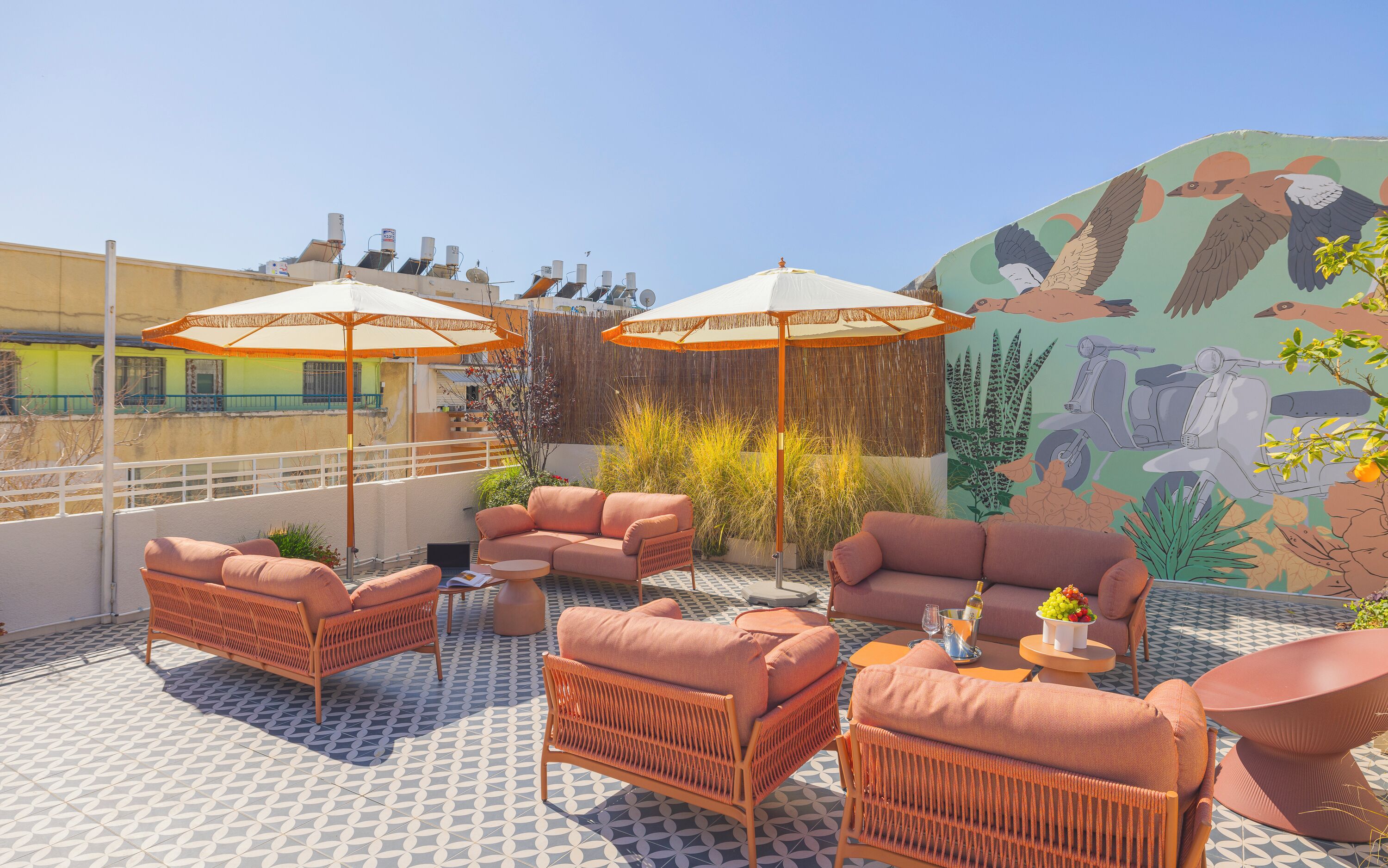 Terraço no telhado com móveis de vime, dois guarda-sóis e um mural de aves e plantas.