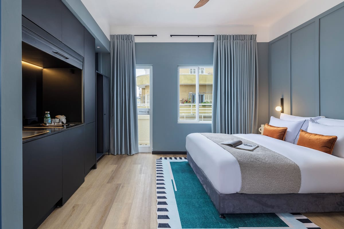 A modern hotel room with a bed, a TV, a desk, and a view of the outside.