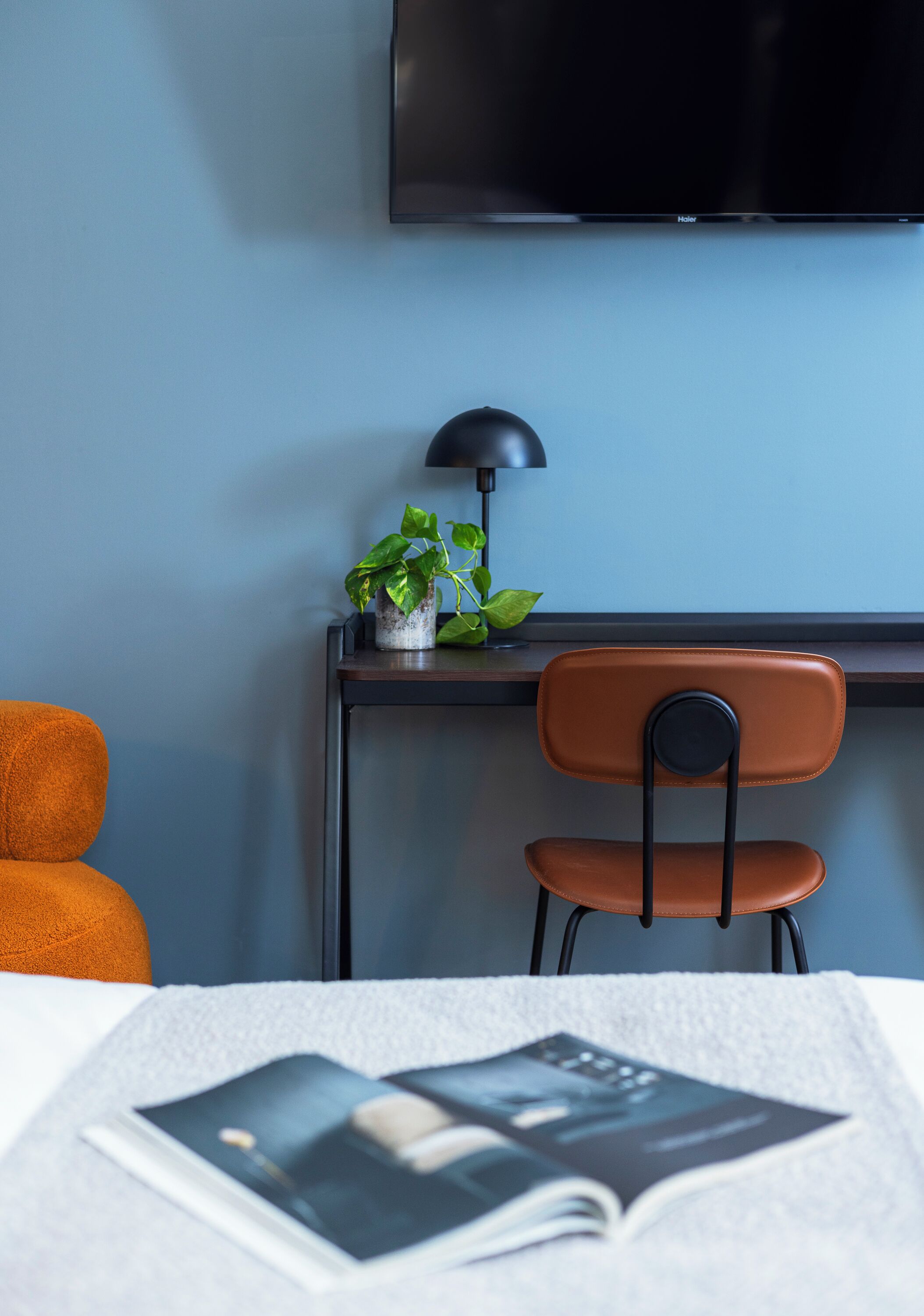 Una habitación con cama, escritorio con silla, televisor, planta y lámpara.