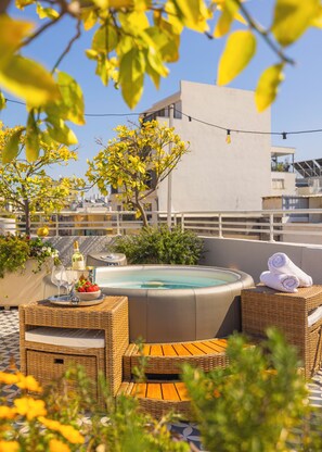 A rooftop terrace with a hot tub, wicker furniture, and a table with a bottle of champagne and strawberries. - Albi Florentin (Tel Aviv)