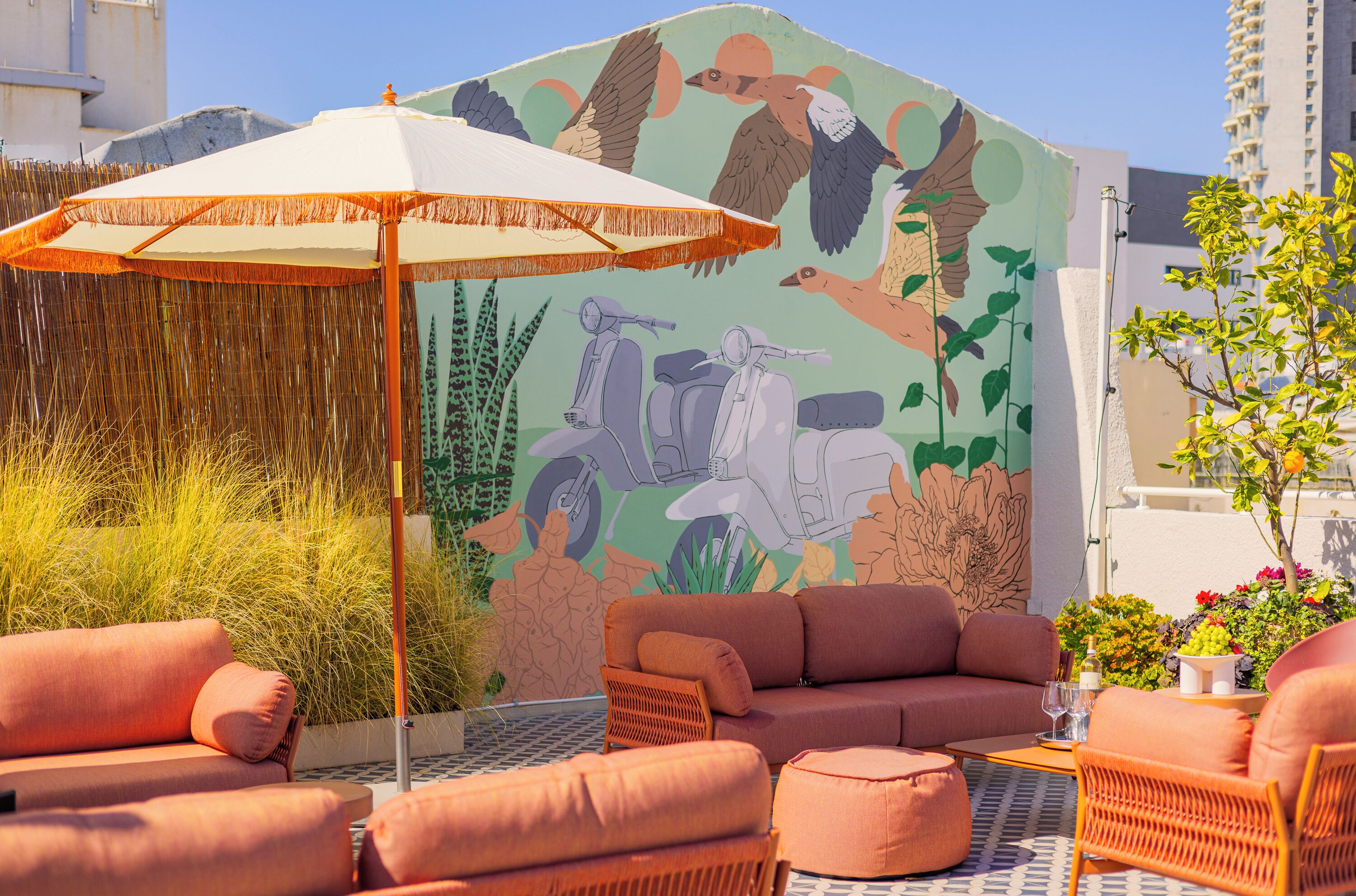 A rooftop lounge with a mural, outdoor seating, and a decorative umbrella.
