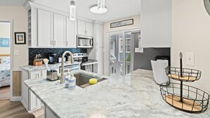 A modern kitchen with white cabinets, a stainless steel microwave, and a large island with a sink. - Escape to Beach Bum 5 - Your Ultimate Family Beach Retreat in Shore Drive (Myrtle Beach)