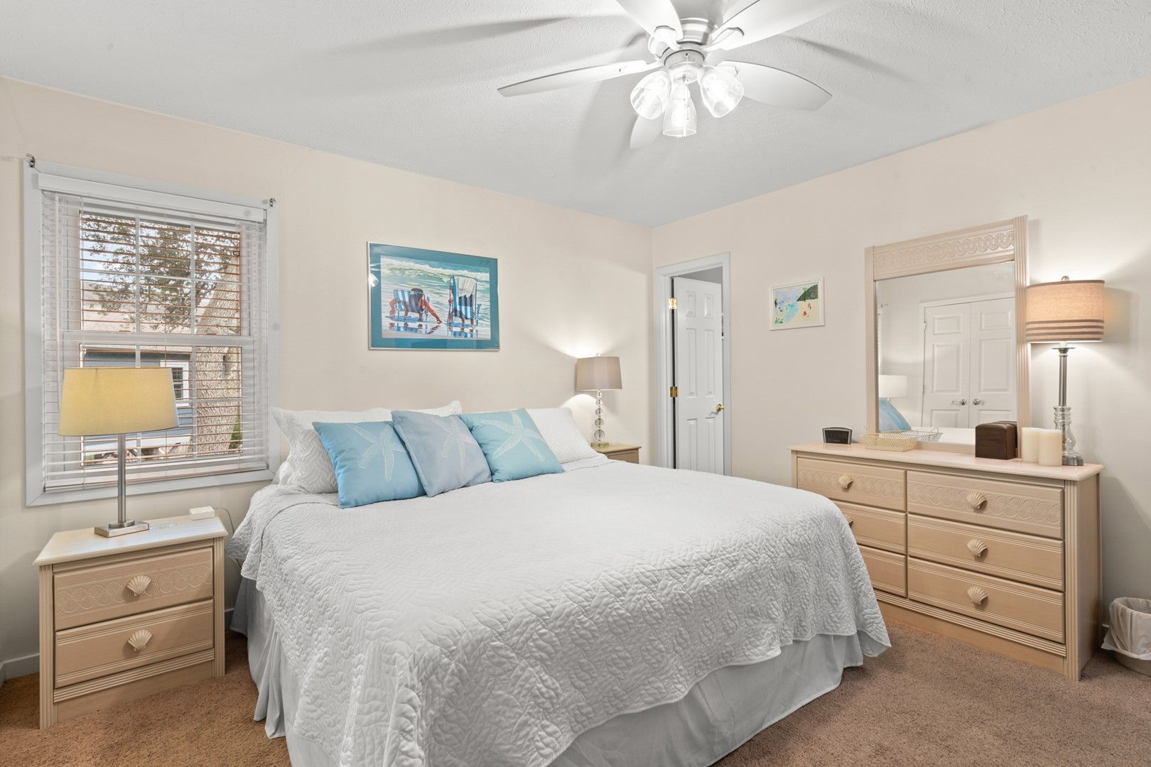 A bedroom with a bed, a nightstand, a dresser, a ceiling fan, and a window with blinds.