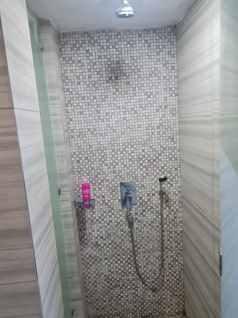 A shower with a tiled wall, a handheld showerhead, and a wall-mounted faucet.