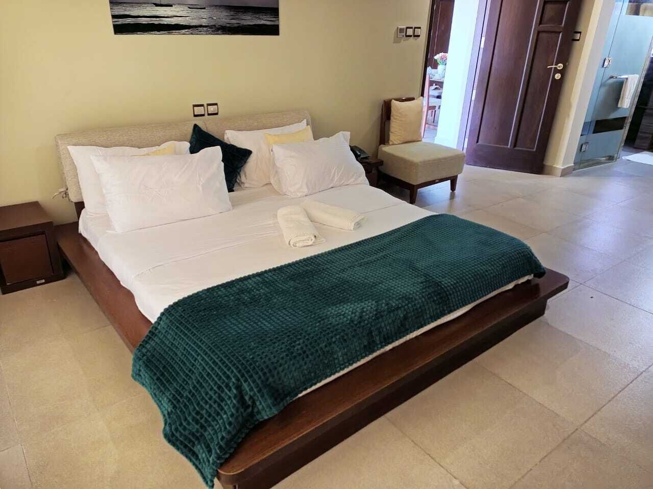 A neatly made bed with white linens and a teal blanket, a wooden headboard, and a nightstand with a lamp.