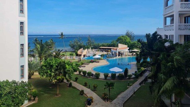A resort with a pool, palm trees, and a view of the ocean. - Luxury Beachfront Apartments (Mombasa)