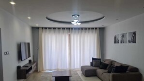 A modern living room with a flat-screen TV, a sofa, a coffee table, and a large window with curtains. - Luxury Beachfront Apartments (Mombasa)