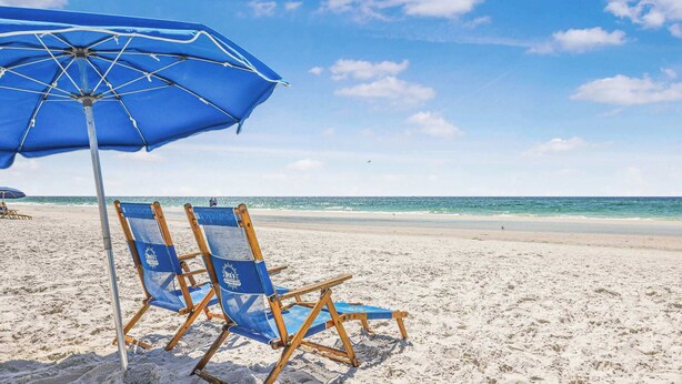 Una playa con una sombrilla azul y dos sillas de playa.