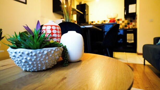 Une table à manger ornée d’une plante en pot, d’un vase blanc et d’une tasse à pois.