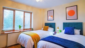 Une chambre d’hôtel avec deux lits, un radiateur, une fenêtre avec des stores et des œuvres d’art encadrées accrochées au mur.