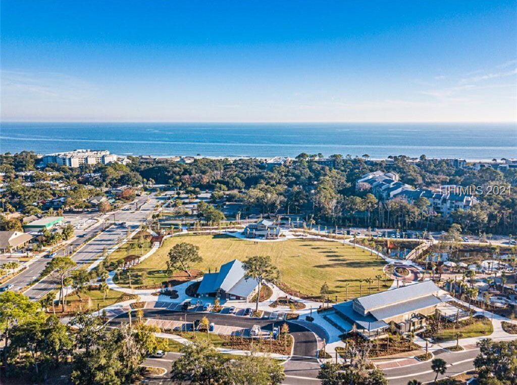 An aerial view of a coastal area with a large open field, buildings, and a road network.