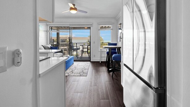 A modern kitchen with a large refrigerator, a dining area with blue chairs, and a view through the glass door.