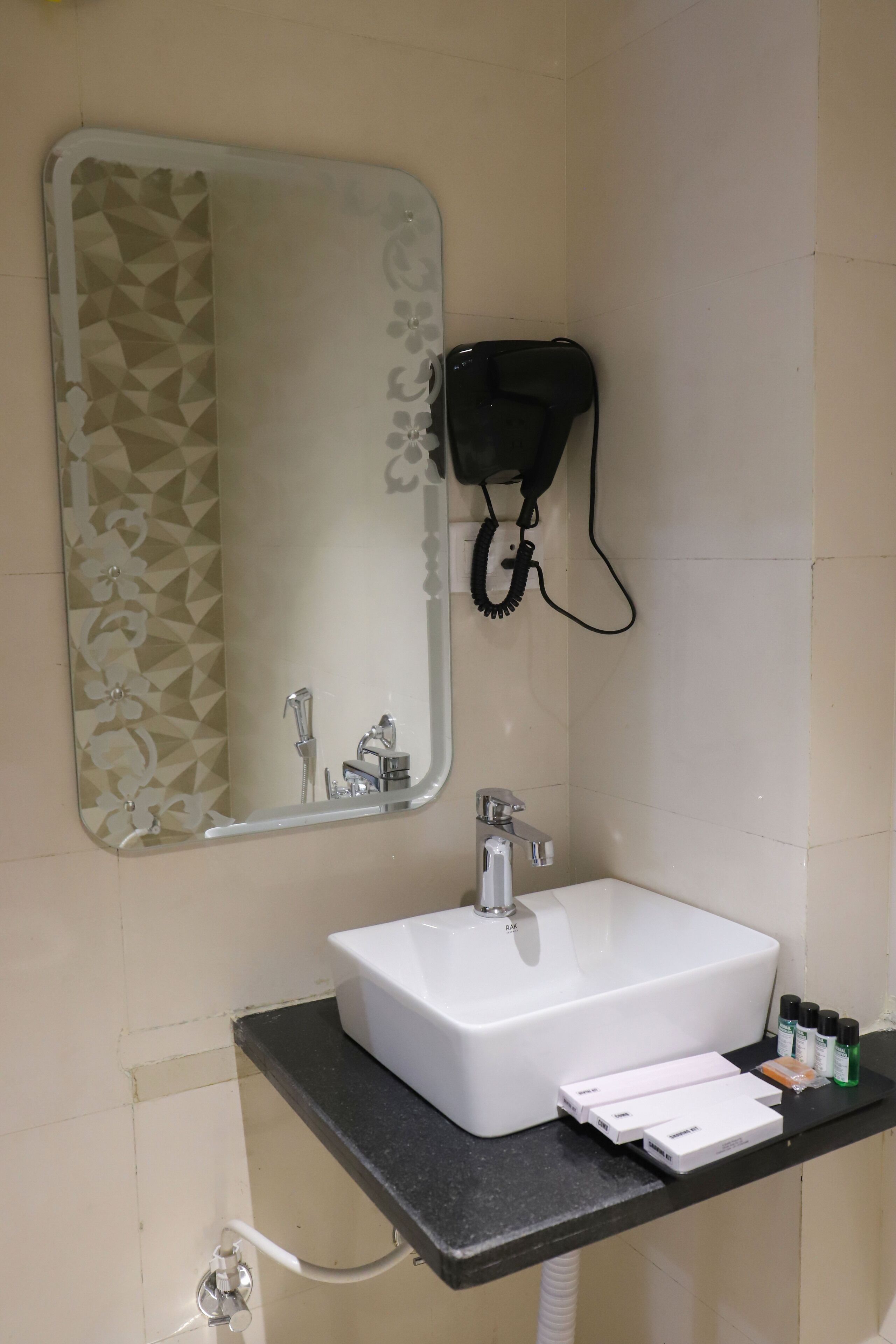 Une salle de bain avec un lavabo blanc, un miroir à motifs géométriques et un sèche-cheveux fixé au mur.