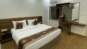 A modern hotel room with a large bed, a ceiling fan, an air conditioning unit, a wooden nightstand, and a wooden dresser with a mirror. - HOTEL GULMOHAR PLAZA BY AUROVILLE ENT (Chandauli)