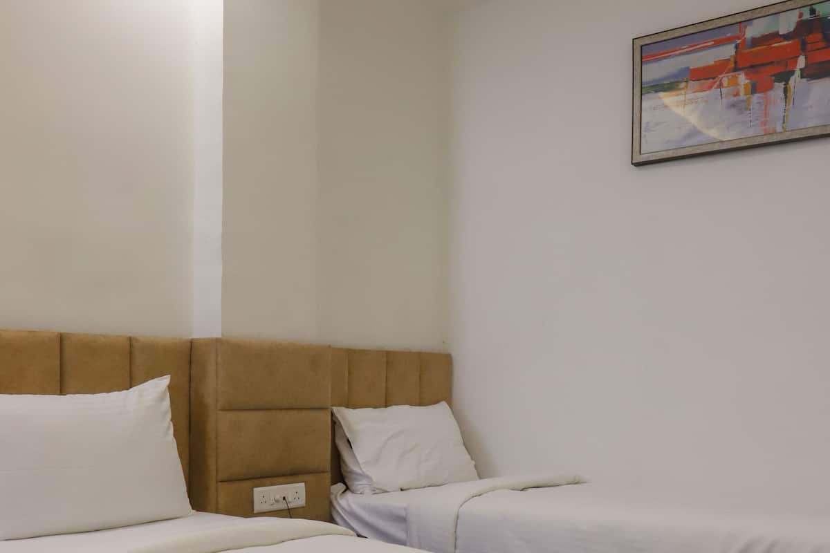 Une chambre d’hôtel avec deux lits simples, une tête de lit, un tableau accroché au mur et un luminaire au plafond.