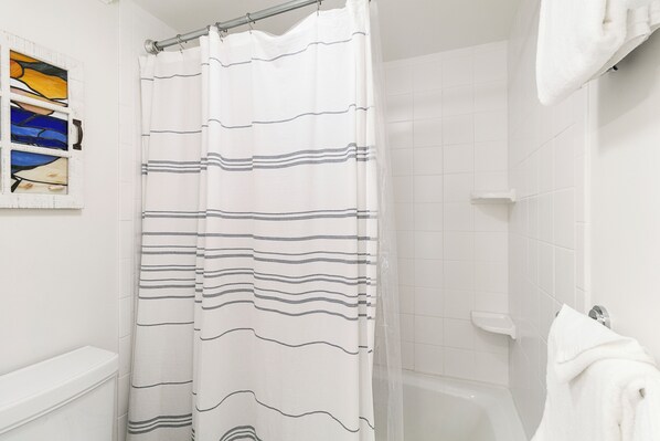 A bathroom with a white tiled wall, a shower curtain with horizontal stripes, a white bathtub, and a towel hanging on the wall.