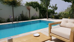 Un espace aménagé au bord de la piscine, avec une table en bois, un coussin et une assiette.