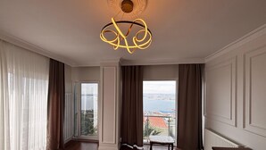 Une pièce spacieuse dotée d’une grande fenêtre donnant sur la ville, d’un plancher en bois et d’un lustre moderne.