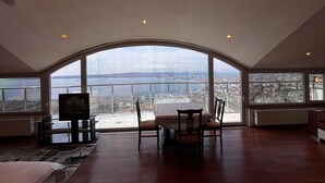 A spacious room with a high ceiling and large windows offering a panoramic view of a cityscape and water.