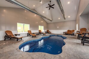 An indoor swimming pool with tiled edges, surrounded by wooden lounge chairs and tables.