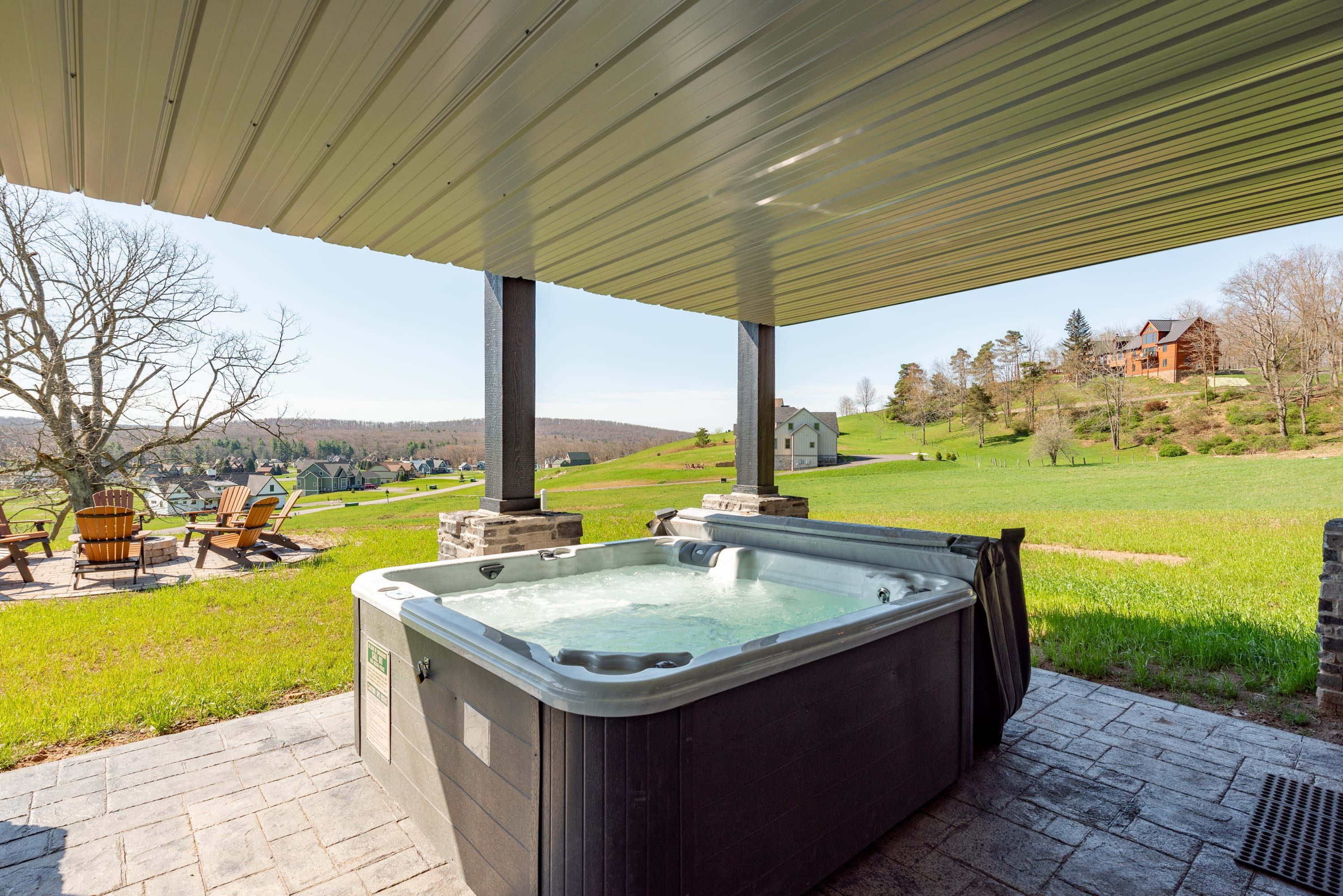 A hot tub under a covered patio with a view of a green landscape and houses in the distance.