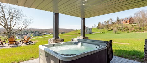 A hot tub under a covered patio with a view of a green landscape and houses in the distance.
