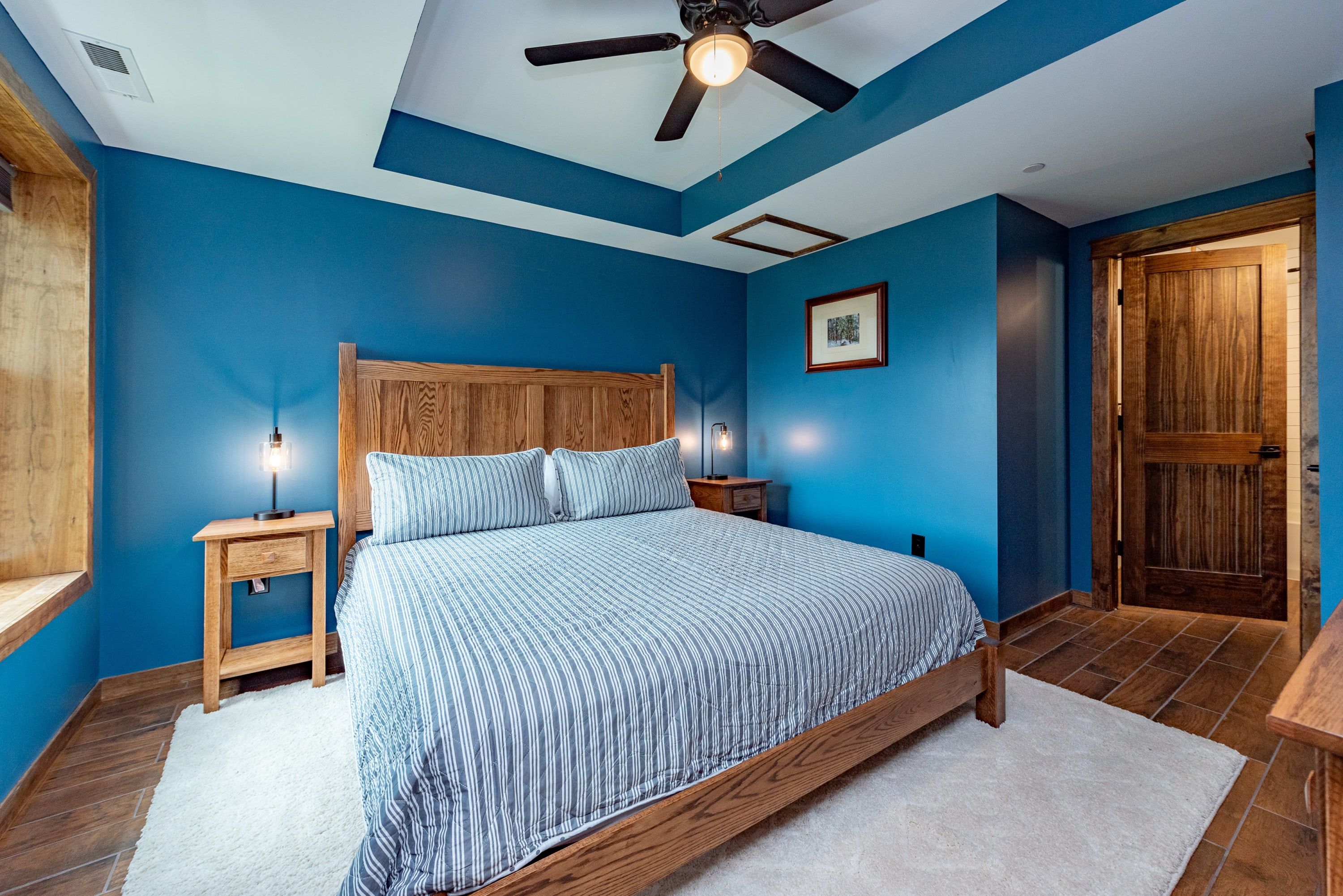 Un dormitorio con cama de madera, una mesita de noche, ventilador de techo y una puerta.