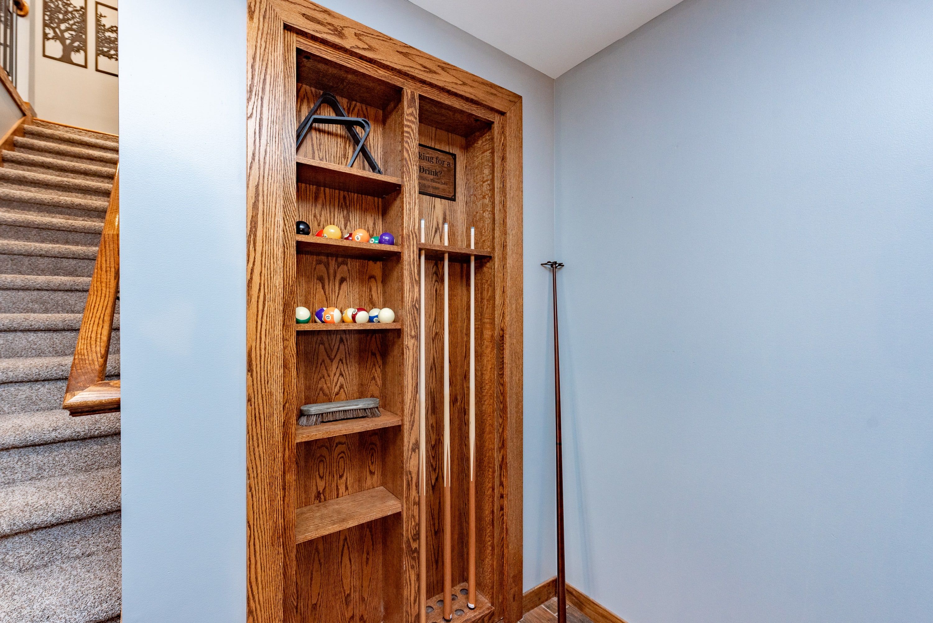 A wooden storage unit with shelves holding pool balls and a cue stick.