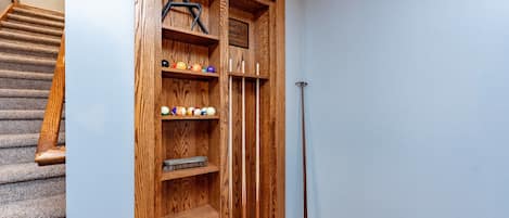 A wooden storage unit with shelves holding pool balls and a cue stick.